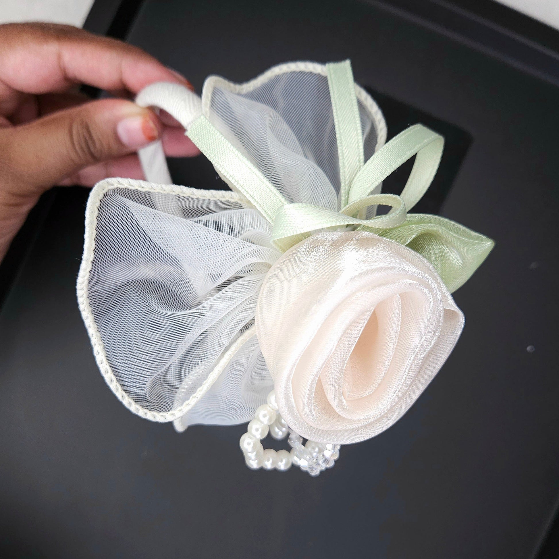 Hand holding a decorative white flower headband with ribbons on a black tray