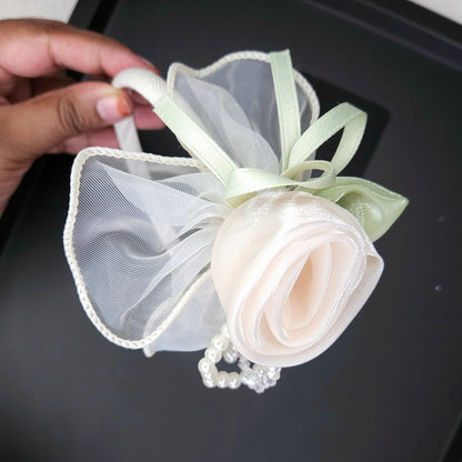 Hand holding a decorative white flower headband with ribbons on a black tray