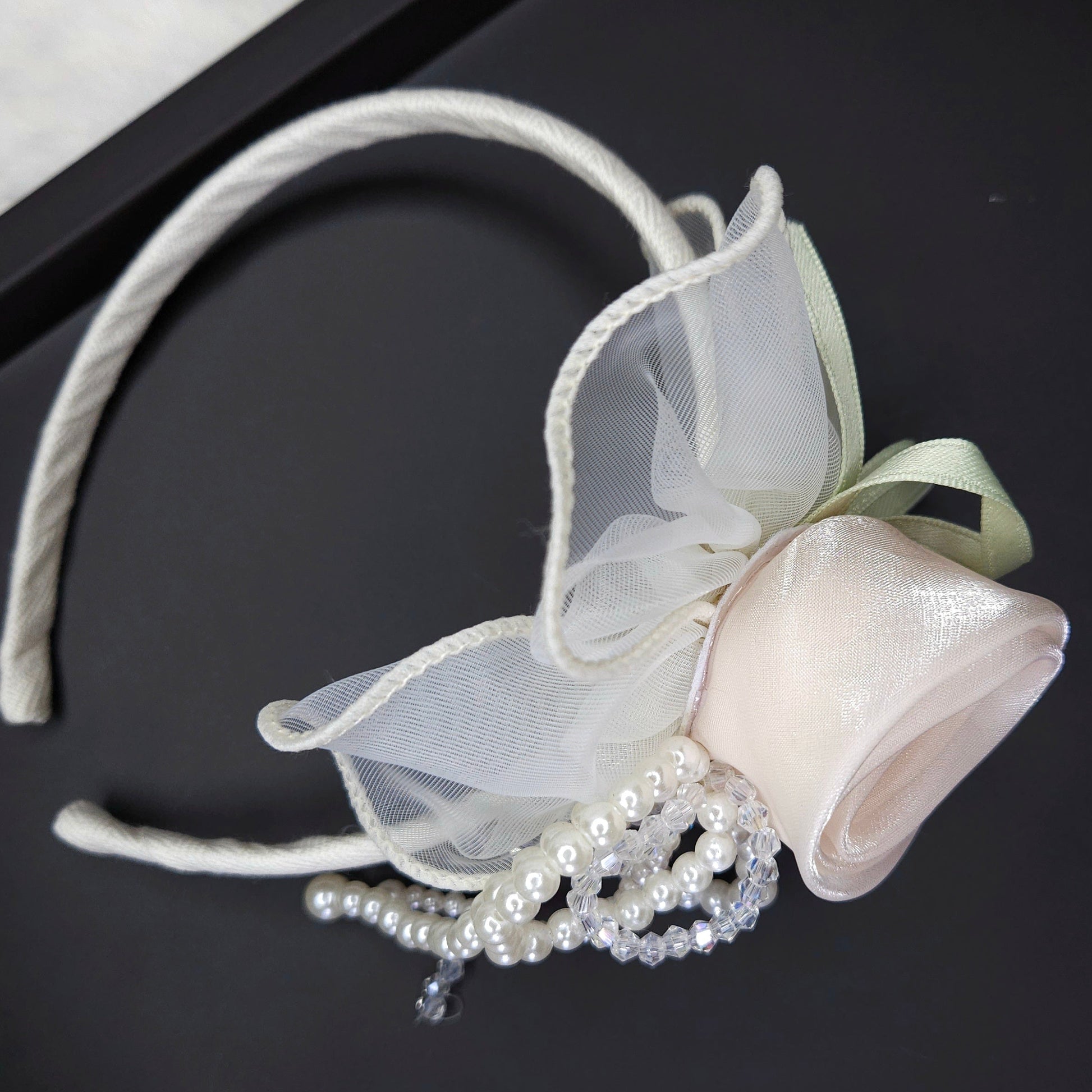 White decorative headband with bow and pearls on a black background