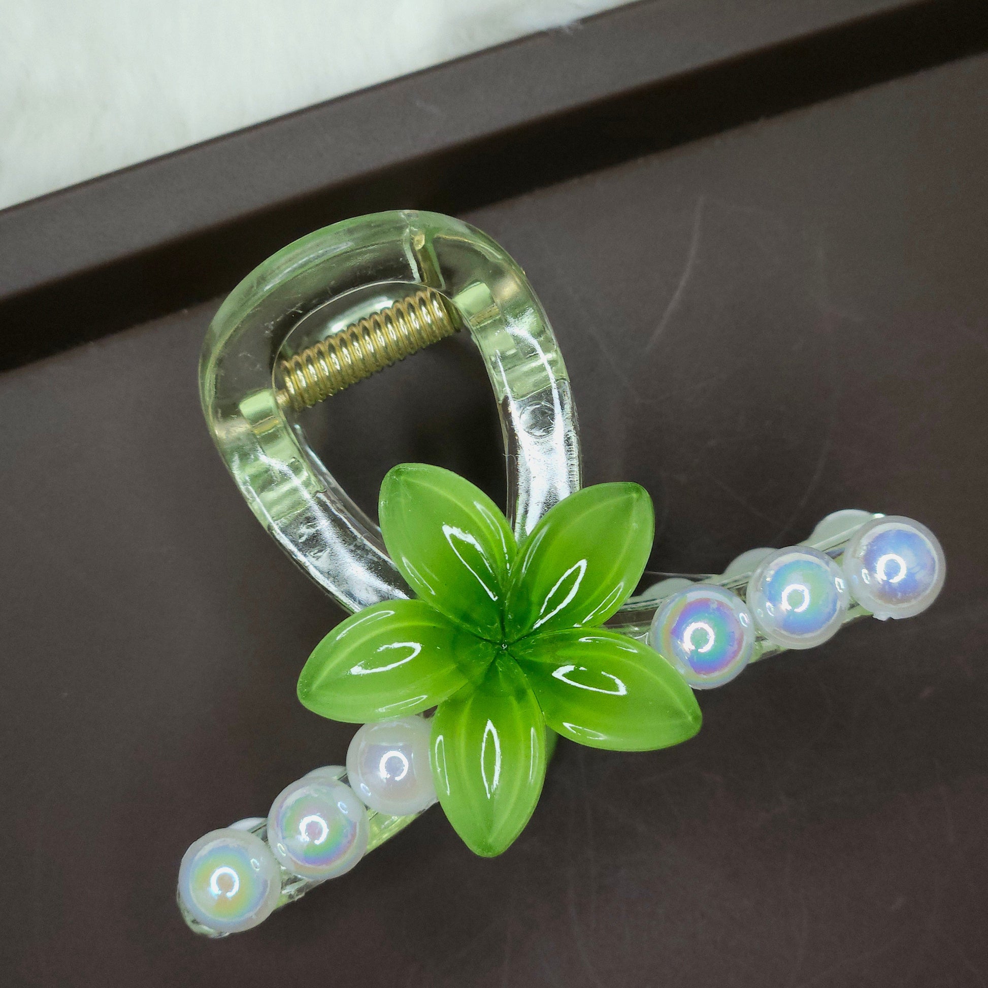 Clear hair claw with a turquoise green flower and a row of small, clear iridescent pearl embellishments.