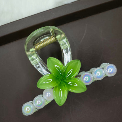 Clear hair claw with a turquoise green flower and a row of small, clear iridescent pearl embellishments.