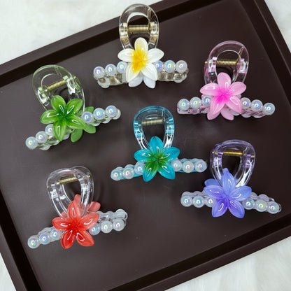 A colorful collection of six clear resin hair claw clips, each decorated with a bright flower and a row of iridescent bubble or pearl beads.