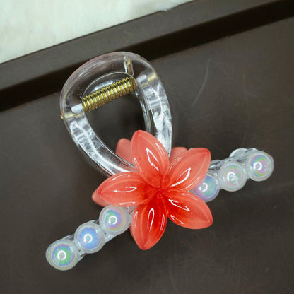 Red-orange flower hair claw clip with a clear plastic base and an accent row of luminous faux pearls.