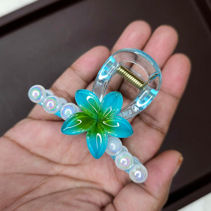 Clear hair claw with a turquoise blue flower and a row of small, clear iridescent pearl embellishments.