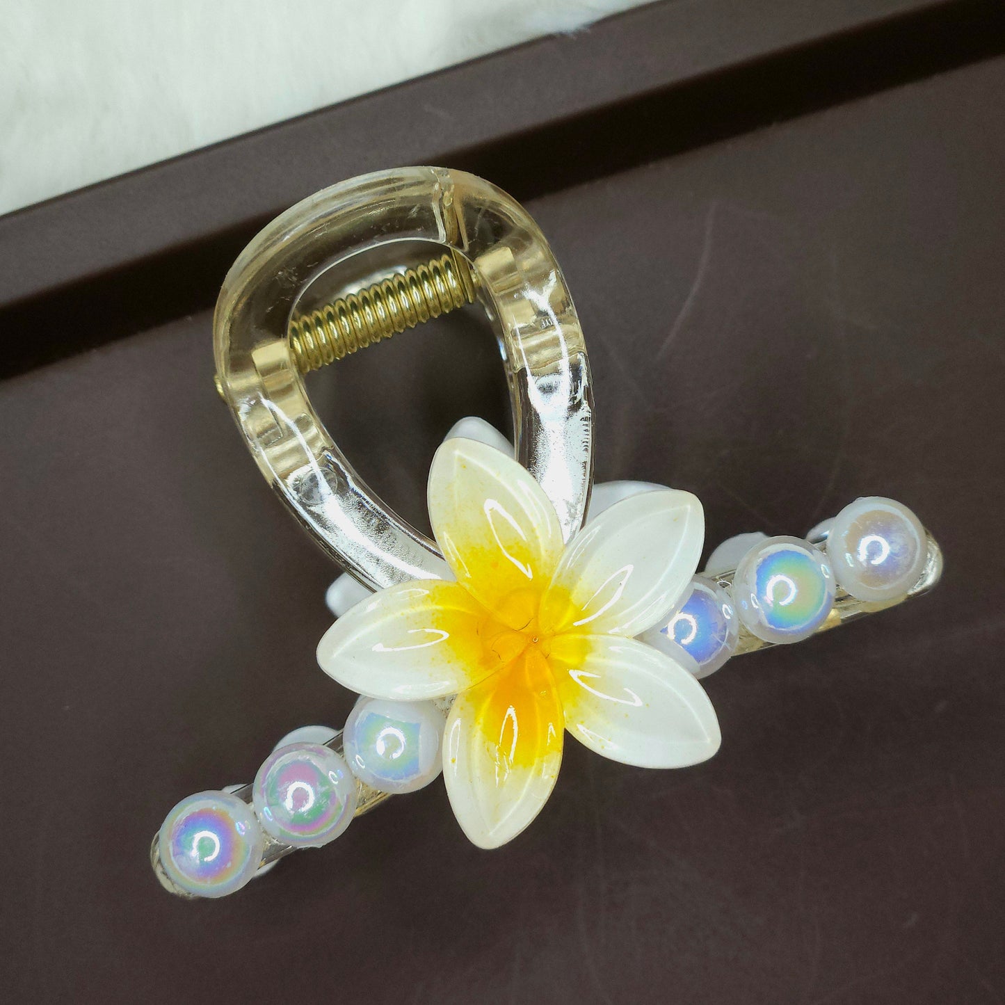 Clear hair claw clip with a white and yellow hibiscus flower and translucent iridescent pearl beads.