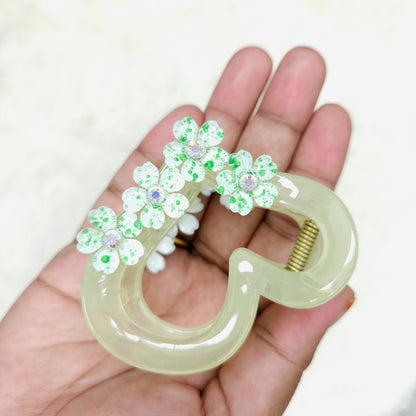 Decorative hair clip with green floral designs held in a hand against a white background