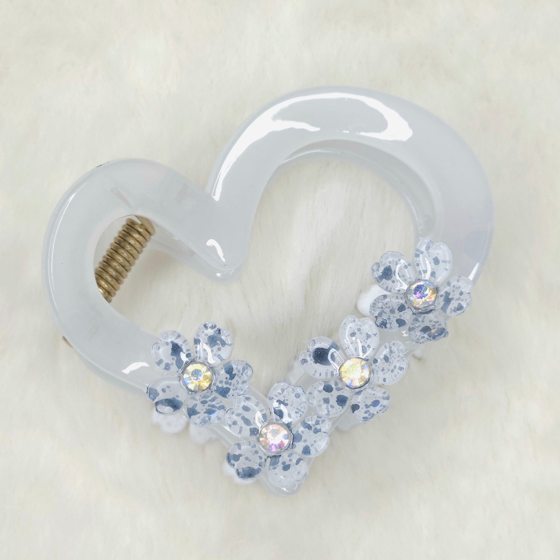 Heart-shaped hair clip with clear resin and embedded crystals on a light background