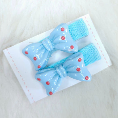 Pair of blue bow hair clips with red buttons on a white background