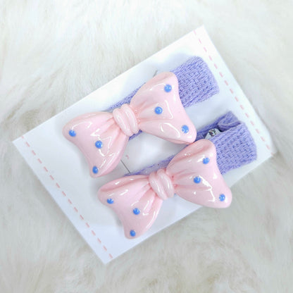 Two pink and purple hair bows with polka dots on a white card against a light gray background.