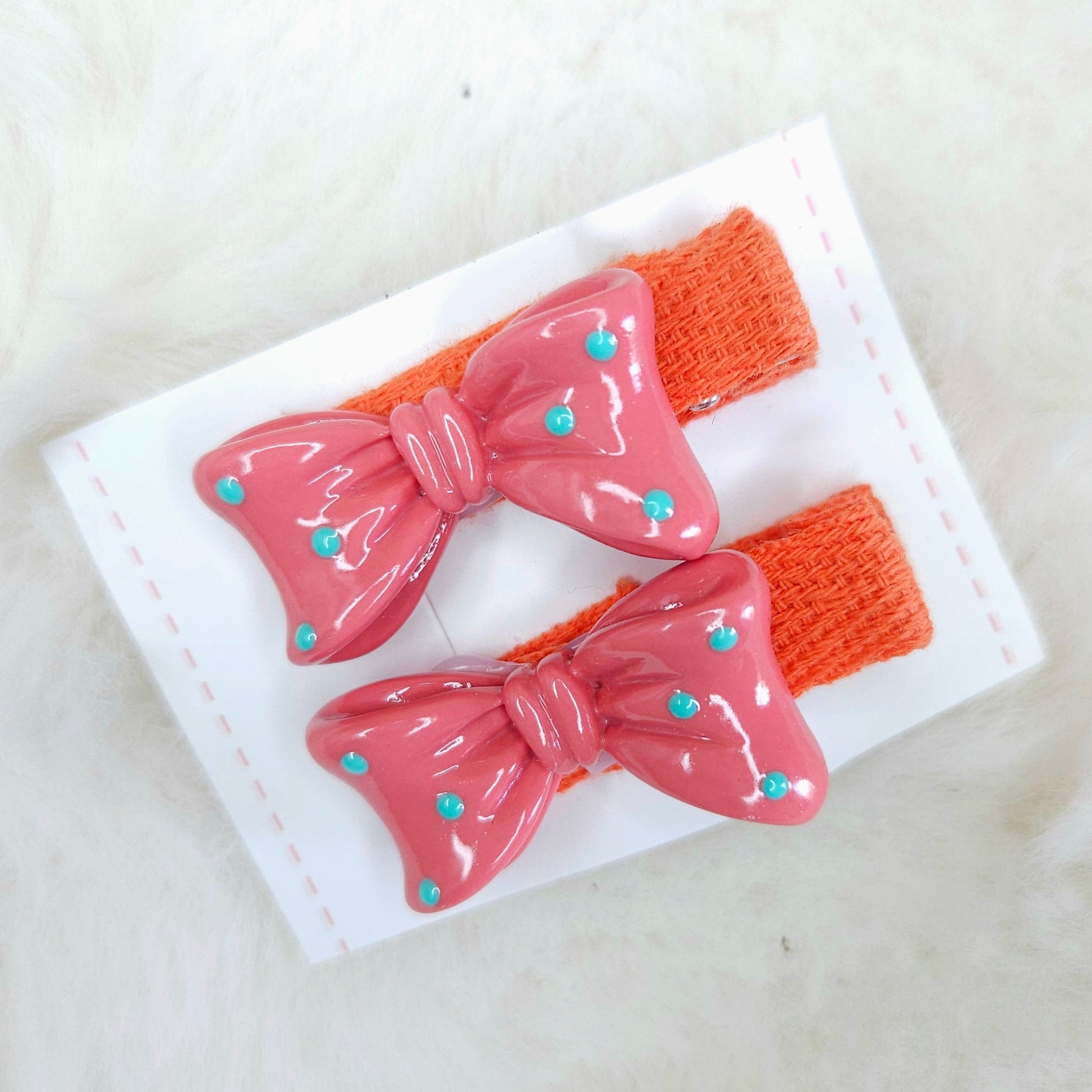 Two pink hair bows with orange straps on a white card against a beige background