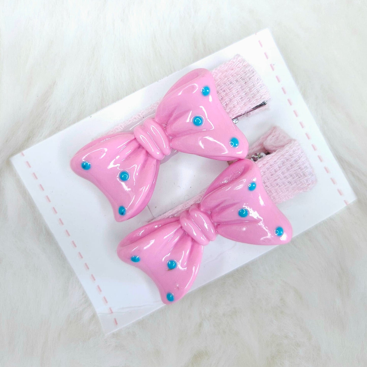 Pink hair bows with blue centers on a white card against a light background