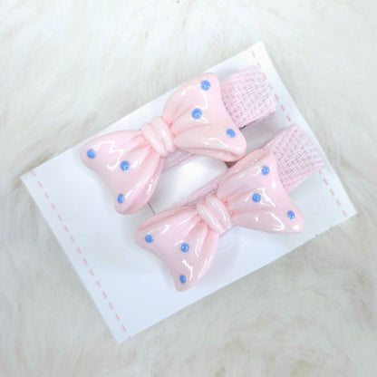Two pink hair bows with blue polka dots on a white card against a white background