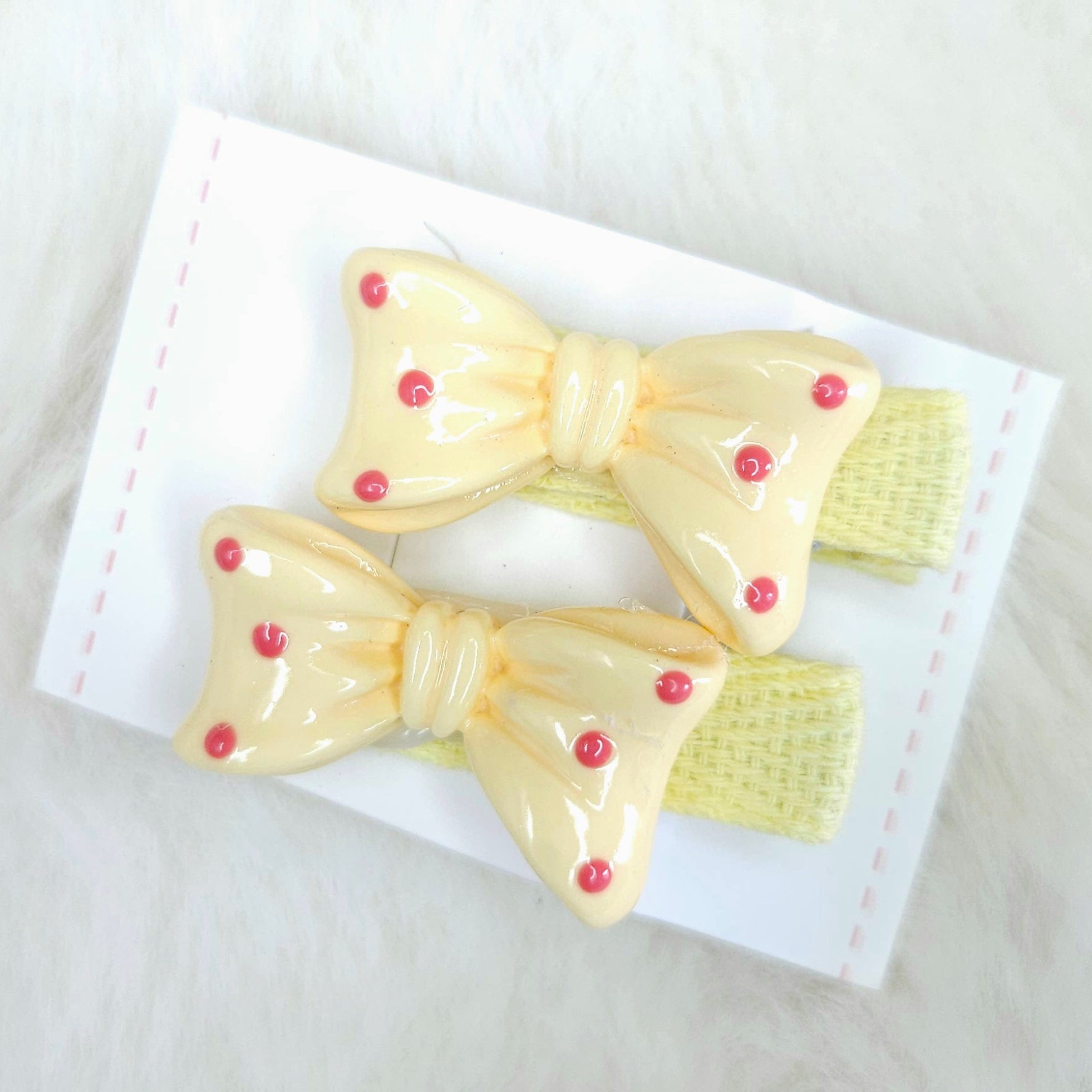 Two yellow hair bows with red centers on a white card against a light background