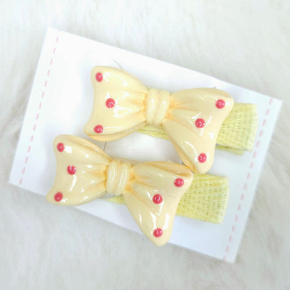 Two yellow hair bows with red centers on a white card against a light background