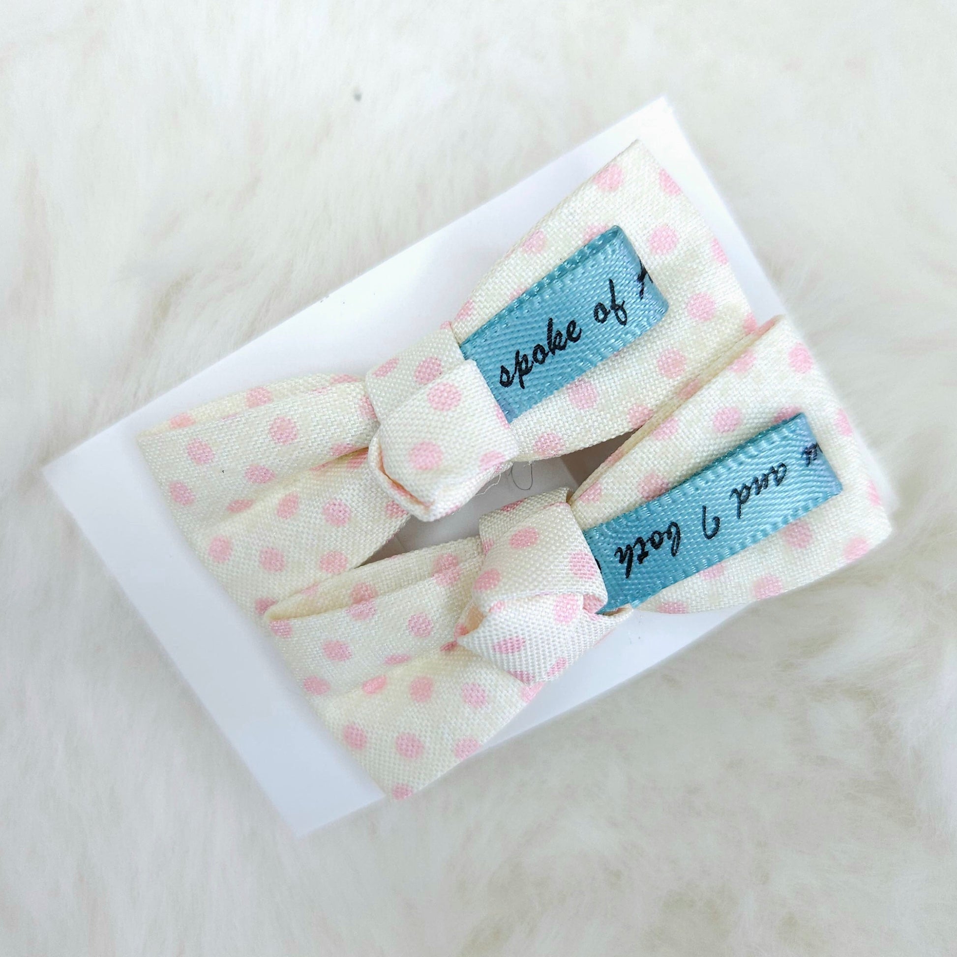Two baby hair bows with polka dot pattern and blue labels on a white background