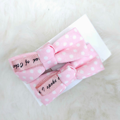 Two pink polka dot hair bows with ribbons on a white background