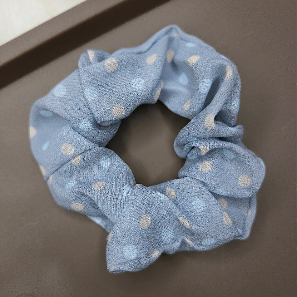 Blue scrunchie with white polka dots on a gray surface