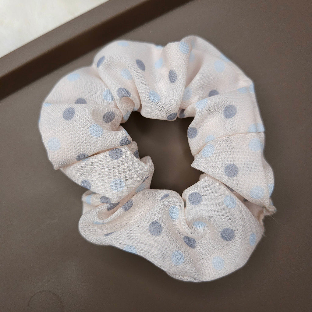 Cream color scrunchie with blue polka dots on a dark surface