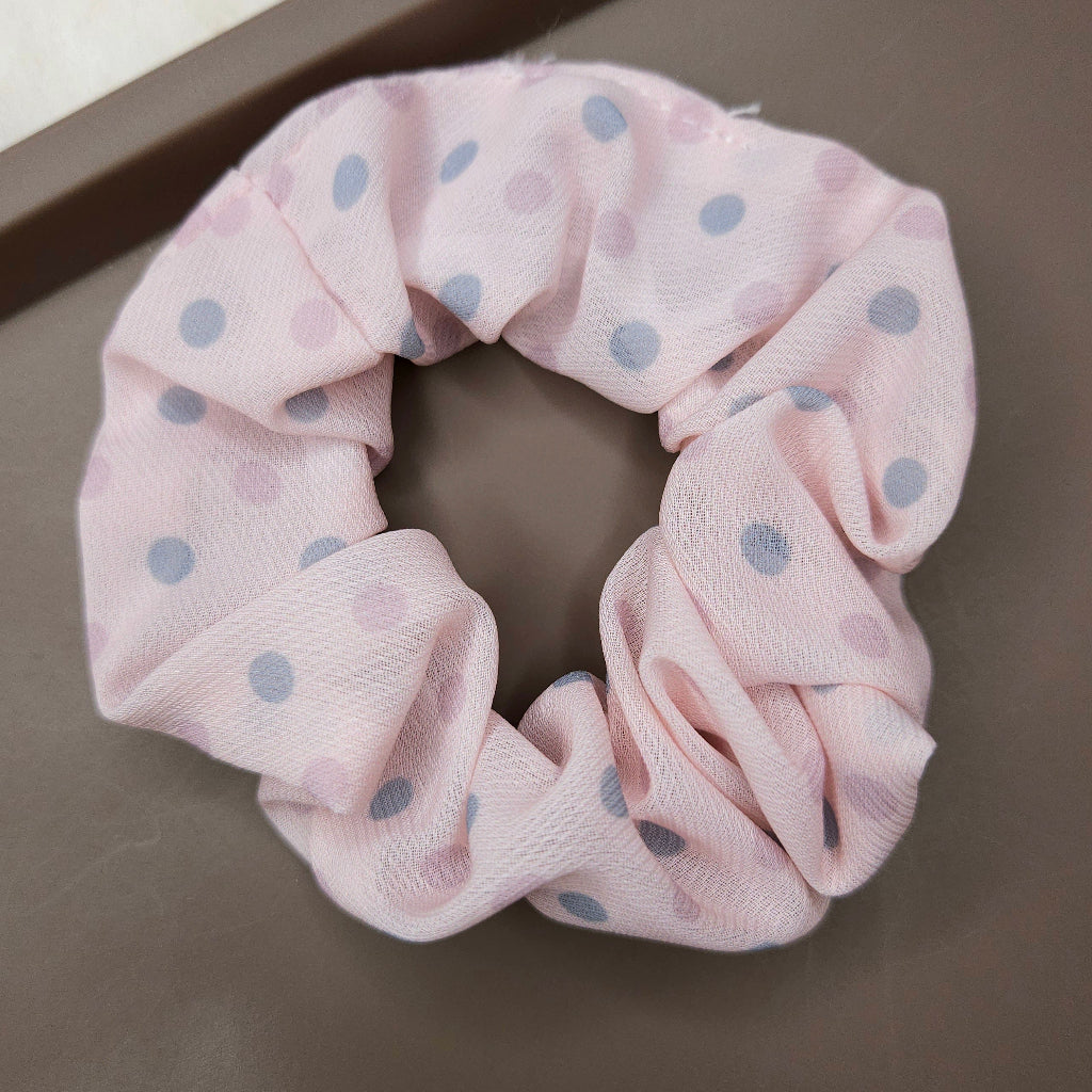 Pink scrunchie with blue polka dots on a dark surface