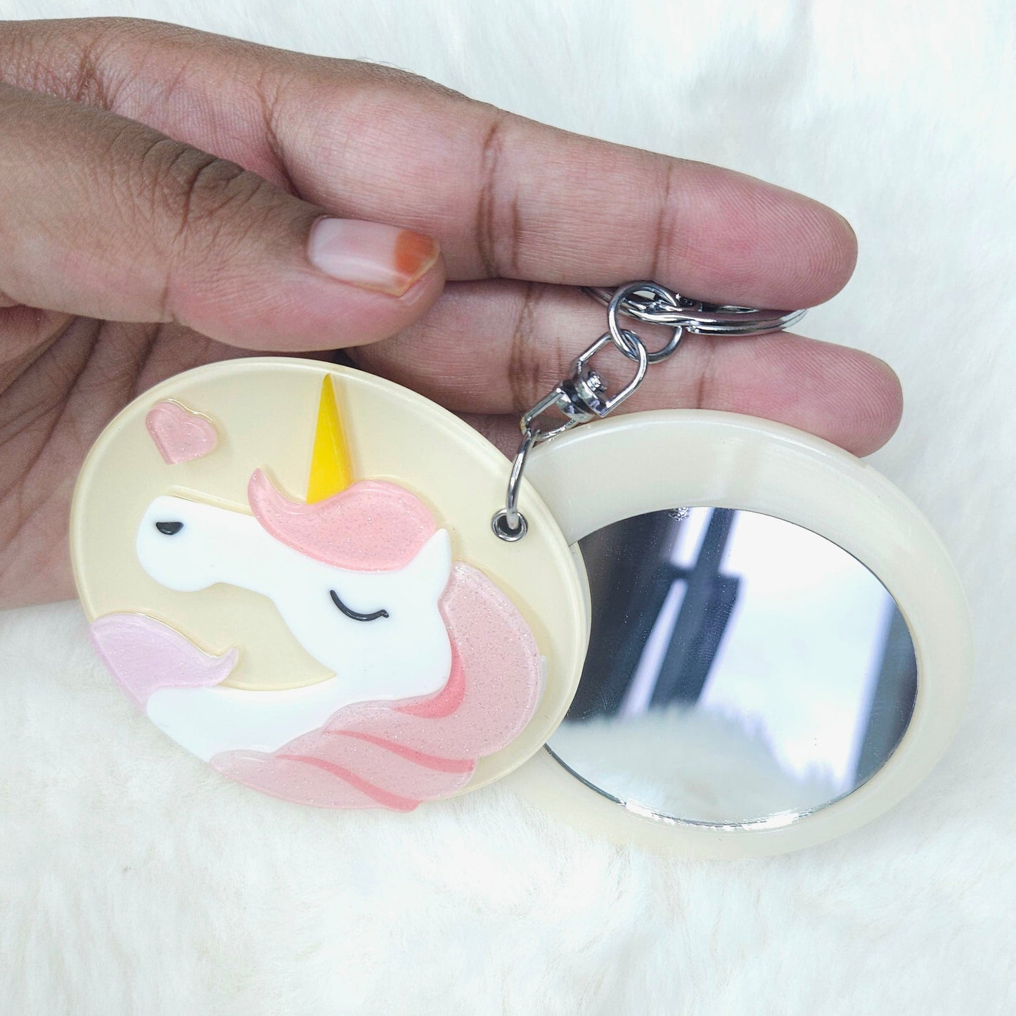 Hand holding a compact mirror with a unicorn design on a white background