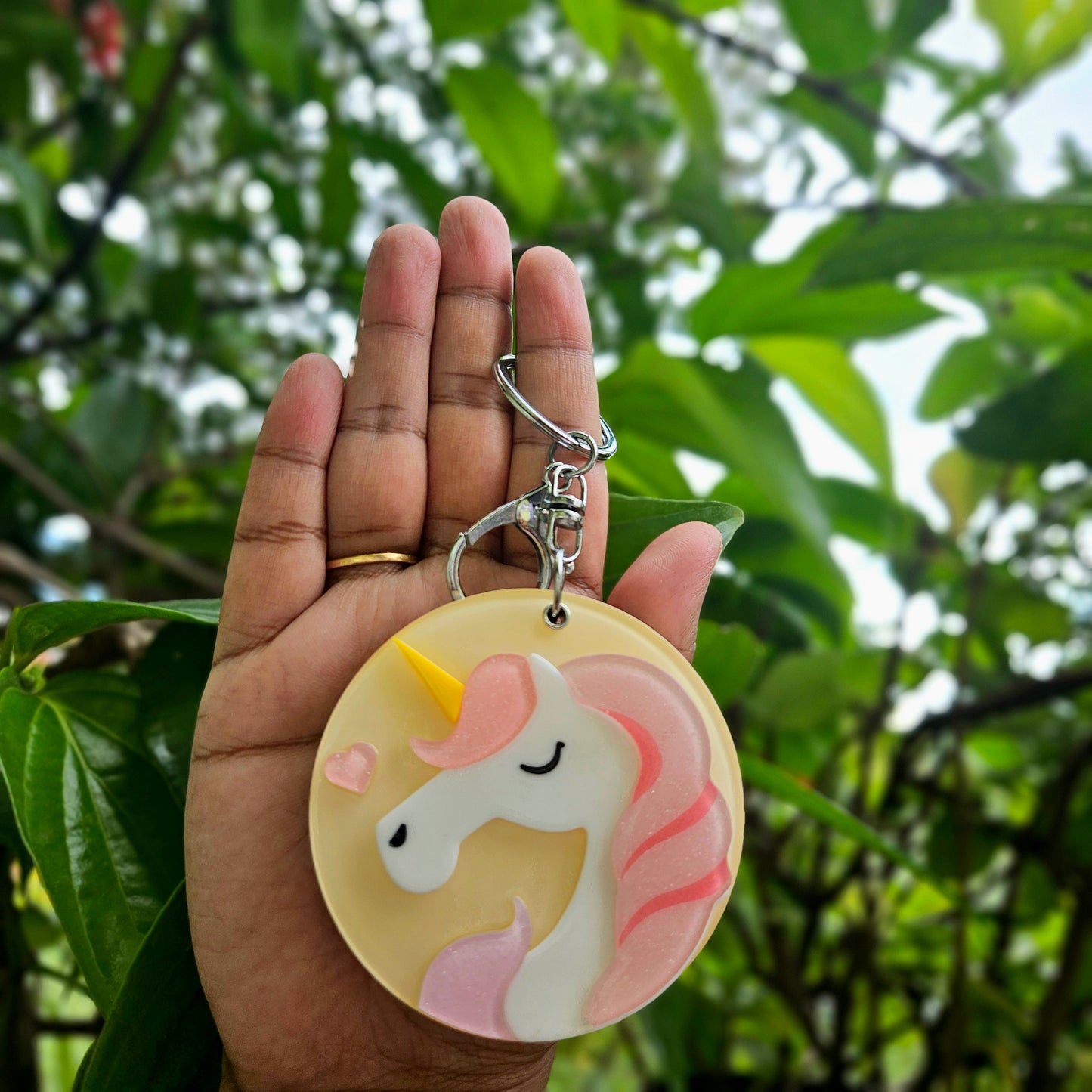 Hand holding a unicorn keychain with a blurred green leafy background