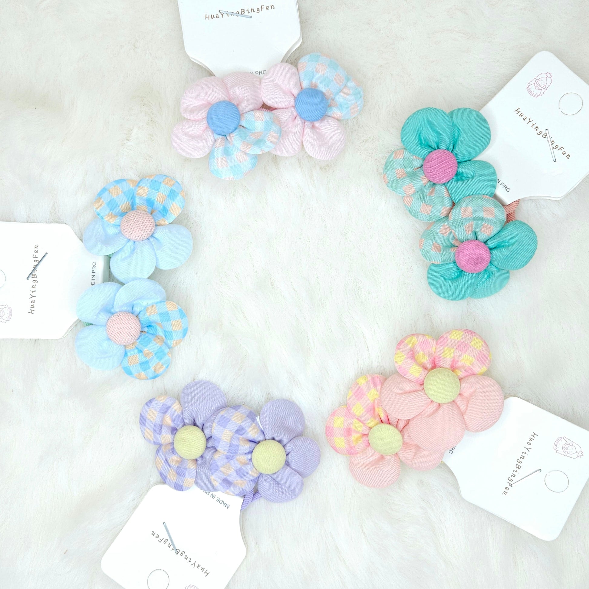 Set of colorful flower-shaped hair ties on a white background with brand tags.