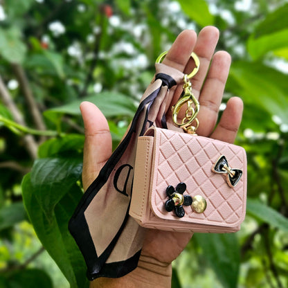 Close-up of a Pink Quilted Faux Leather Mini Key Pouch. The front features a gold-tone snap, a black enamel bow, and a cluster of black floral charms. It includes a gold keyring and a patterned satin scarf/ribbon.