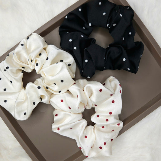 Three polka dot scrunchies in black, white, and cream on a brown tray.