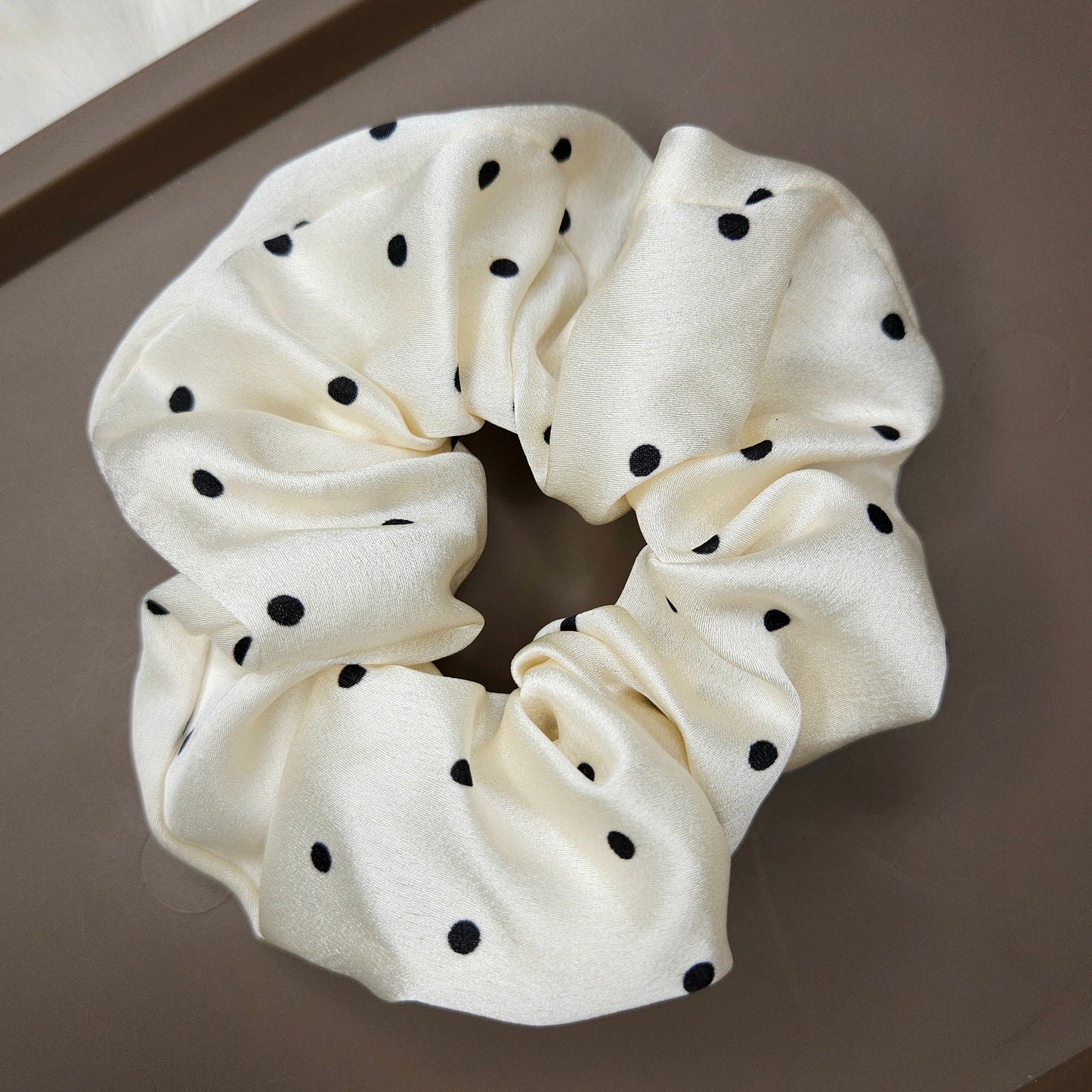 White scrunchie with black polka dots on a brown surface