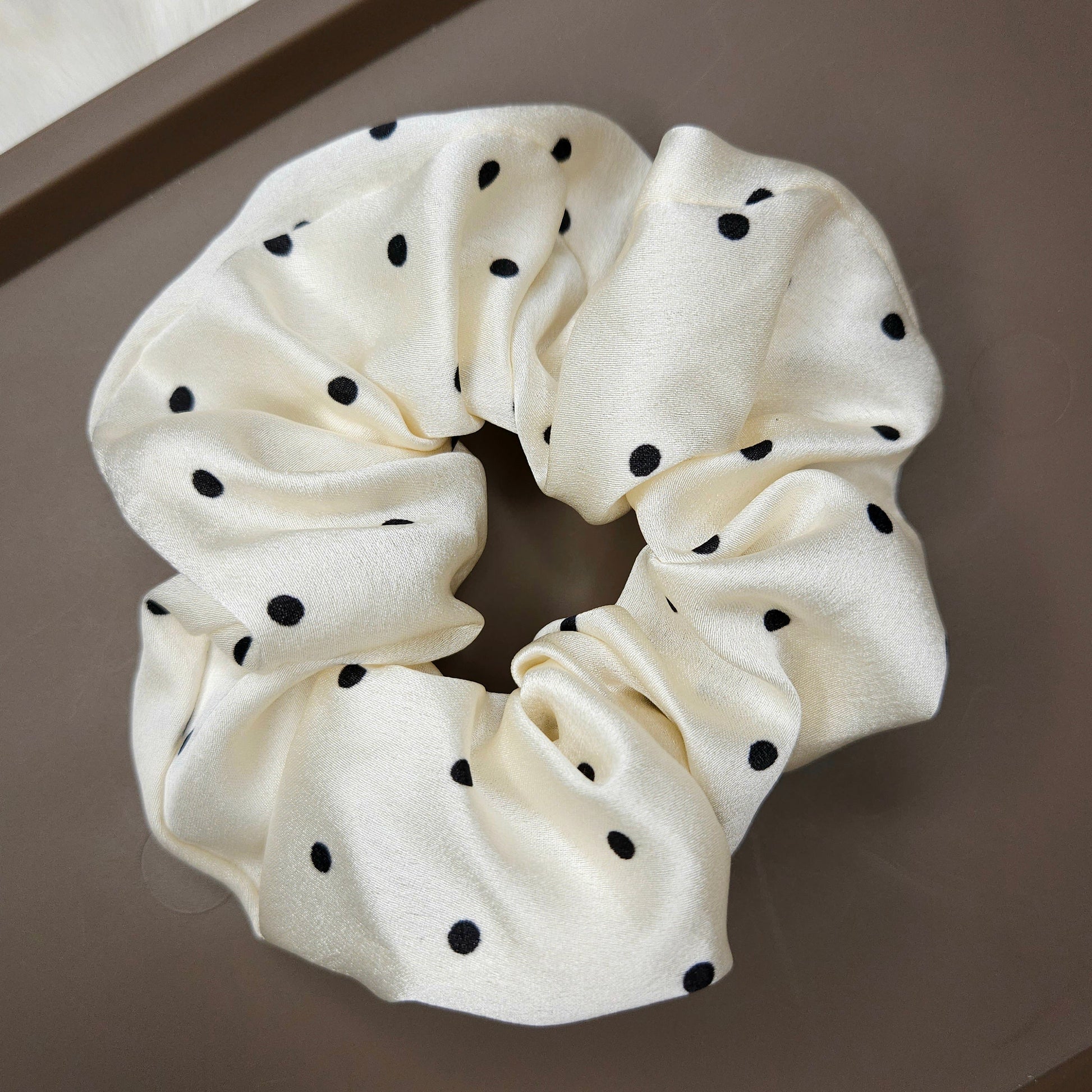 White scrunchie with black polka dots on a brown surface