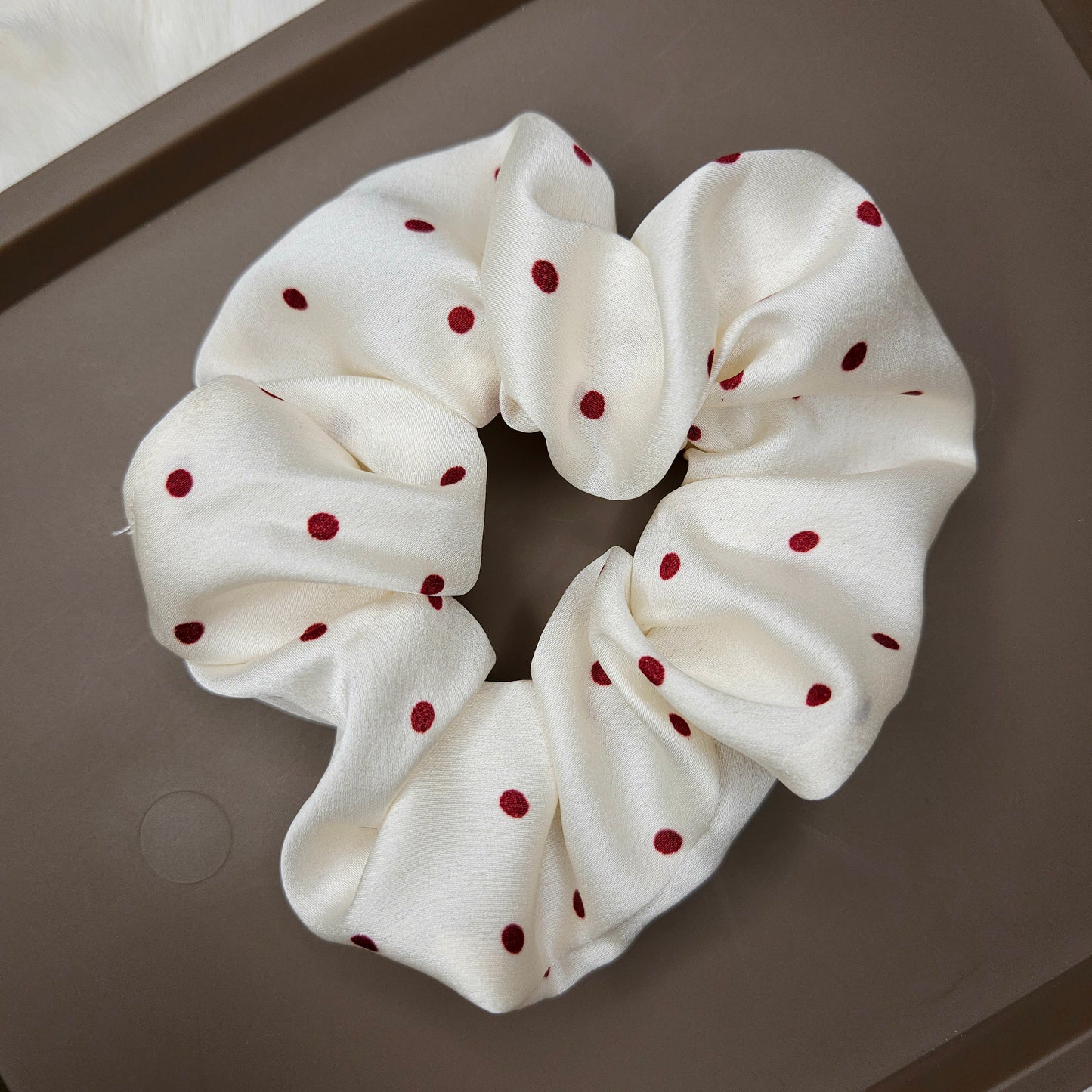 White scrunchie with red polka dots on a gray surface
