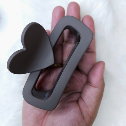 Hand holding a gray metal heart-shaped object against a white background