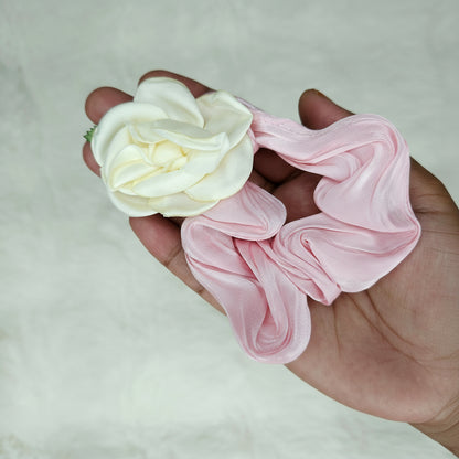 Hand holding a pink scrunchie with a white flower attachment against a neutral background