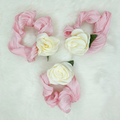 Three pink scrunchies with white flowers on a light gray background