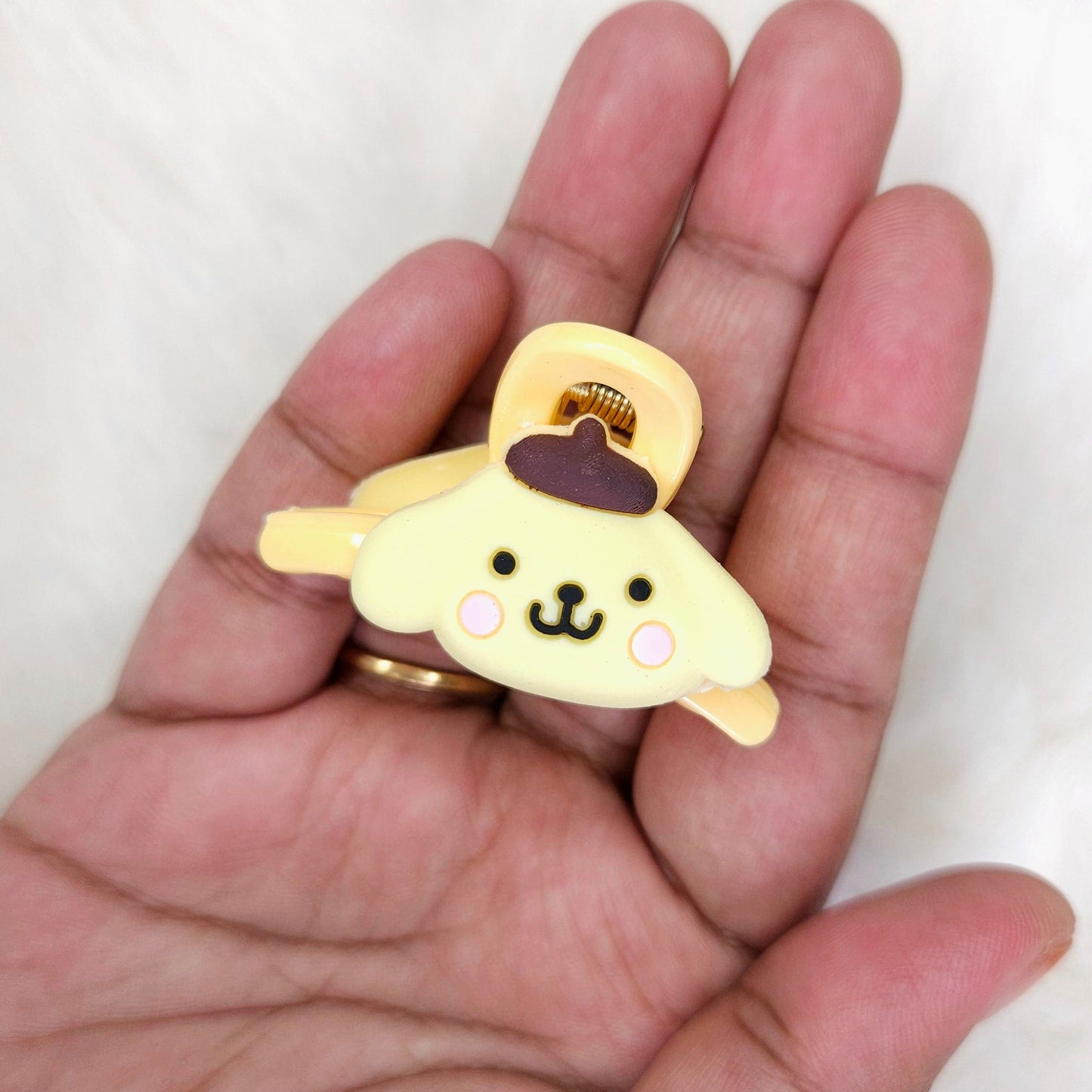 Hand holding a small yellow character hair claw clip with a purple hat on a white background