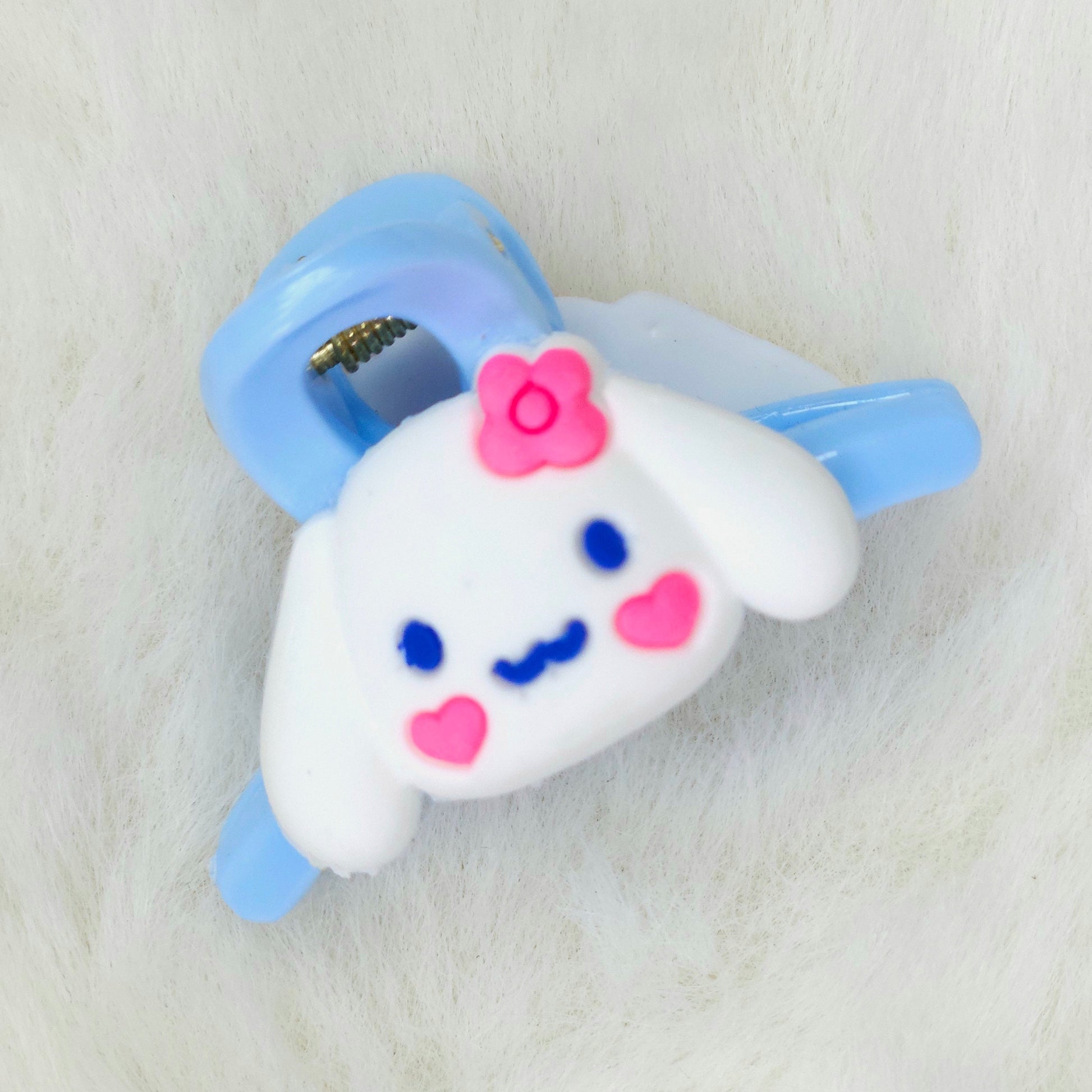 Cute cartoon character hair clip with a white face, blue eyes, pink cheeks, and a blue bow on a light gray background.