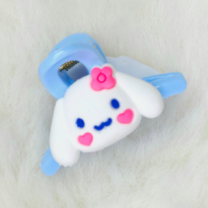 Cute cartoon character hair clip with a white face, blue eyes, pink cheeks, and a blue bow on a light gray background.