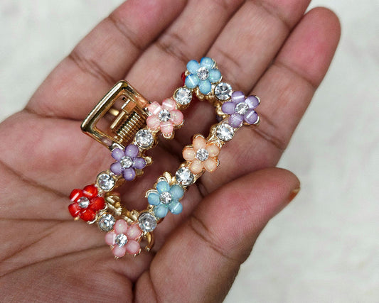 Colorful floral hair clip on a hand against a neutral background
