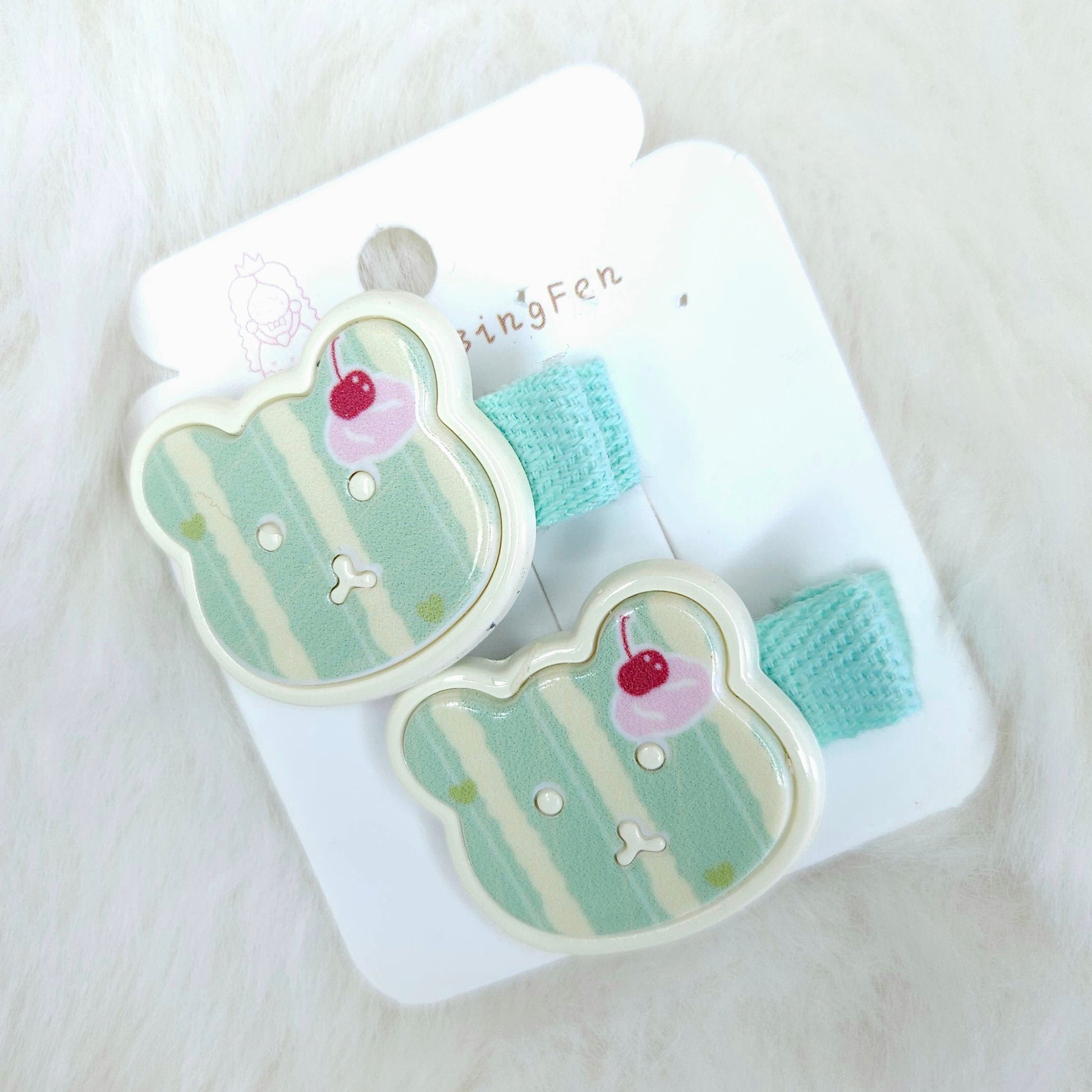Pair of teddy-shaped hair clips with cherry details on a white card against a white background