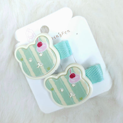 Pair of teddy-shaped hair clips with cherry details on a white card against a white background