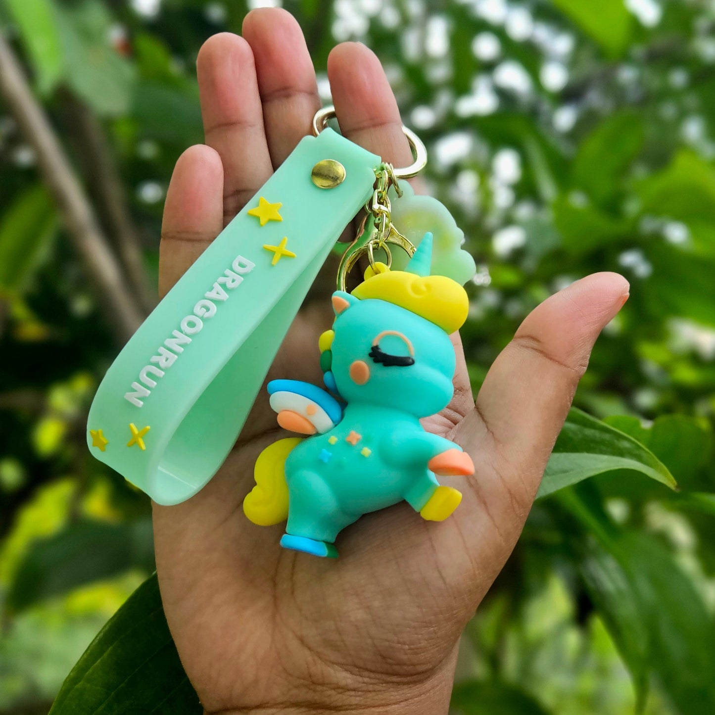 Hand holding a turquoise keychain with a small creature figure against a green leafy background