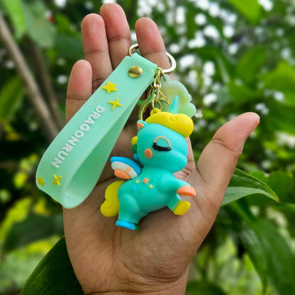 Hand holding a turquoise keychain with a small creature figure against a green leafy background