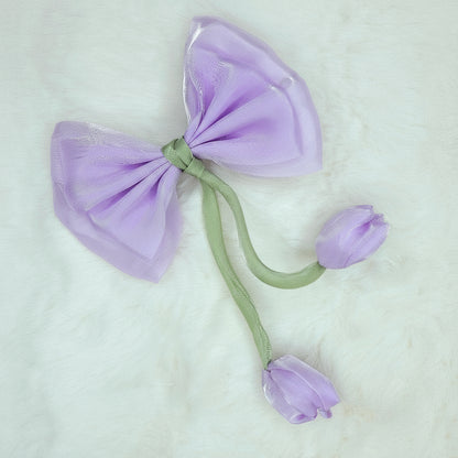 Close-up of a sheer lavender fabric bow with two pale purple fabric tulip buds dangling from a green stem.