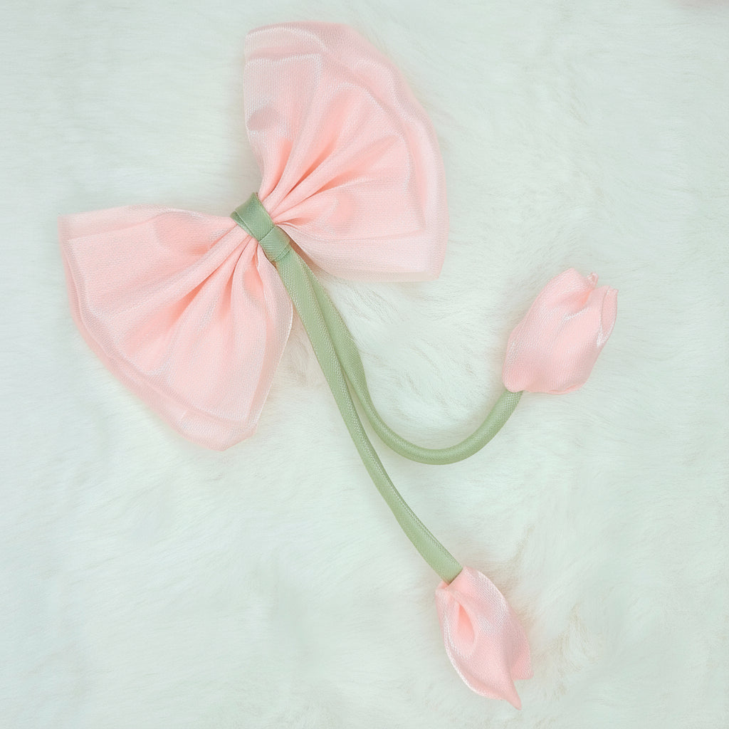 Close-up of a sheer light pink fabric bow with two light pink fabric tulip buds dangling from a green stem.