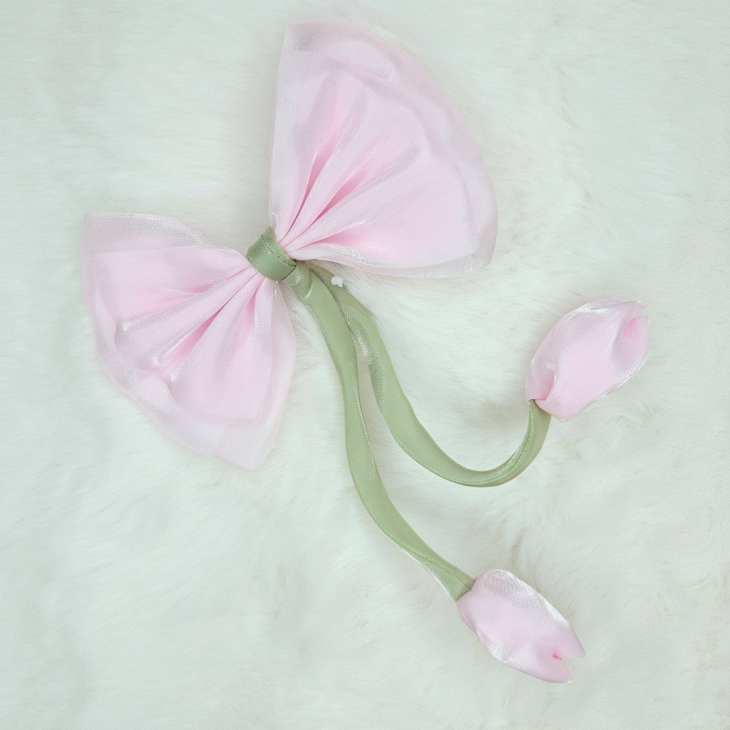 Close-up of a sheer medium pink fabric bow with two medium pink fabric tulip buds dangling from a green stem.