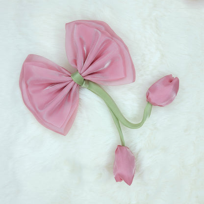 Close-up of a sheer medium pink fabric bow with two medium rose fabric tulip buds dangling from a green stem.