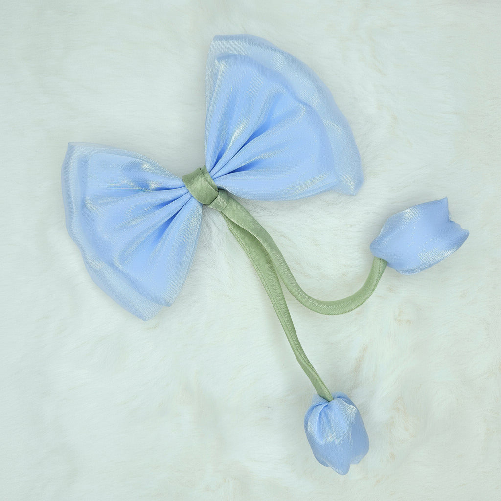 Close-up of a sheer light blue fabric bow with two light blue fabric tulip buds dangling from a green stem.