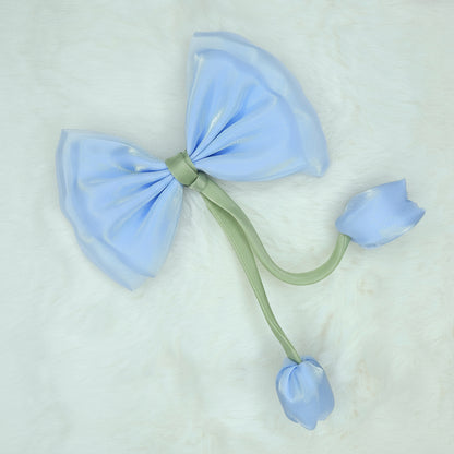 Close-up of a sheer light blue fabric bow with two light blue fabric tulip buds dangling from a green stem.