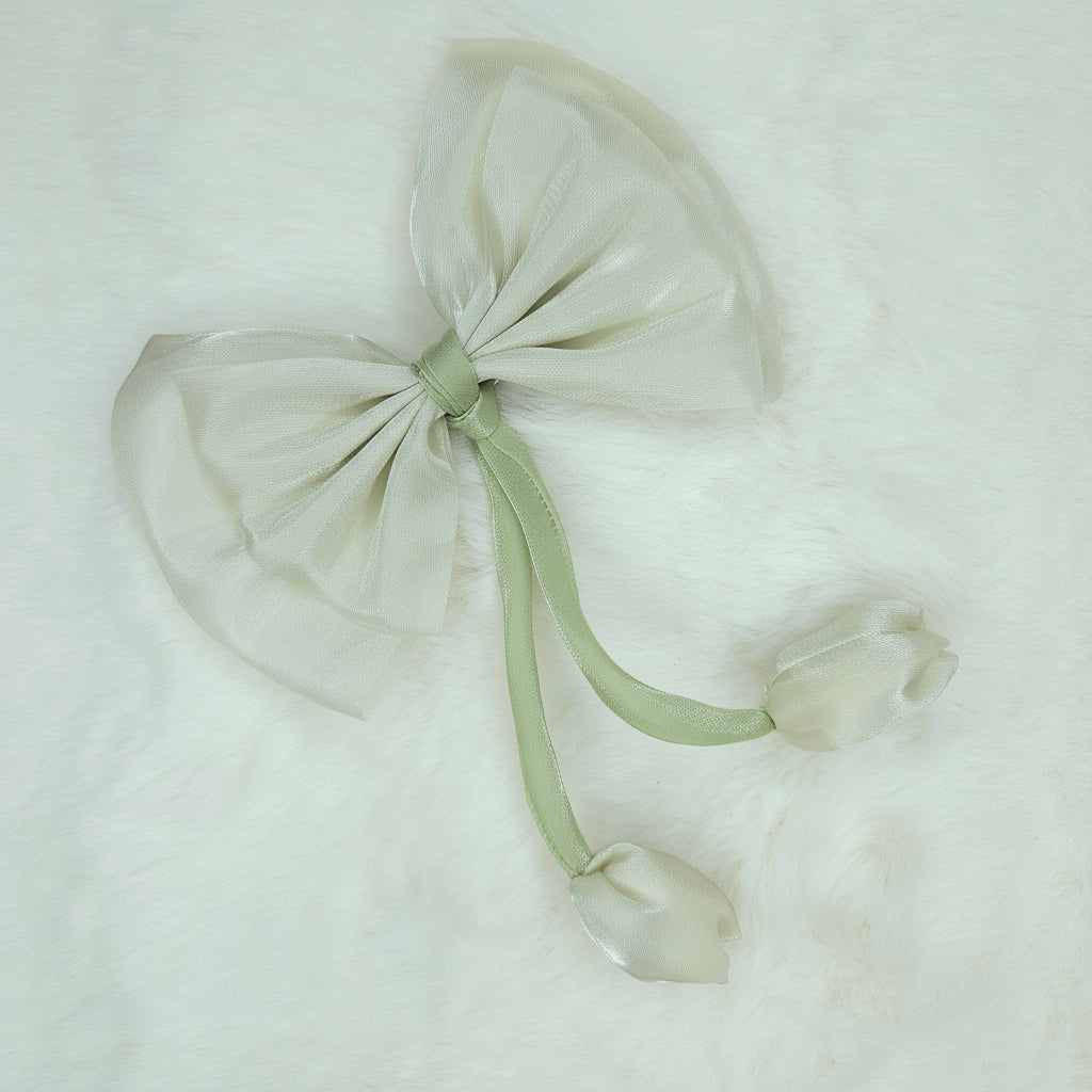 Close-up of a sheer cream fabric bow with two cream fabric tulip buds dangling from a green stem.