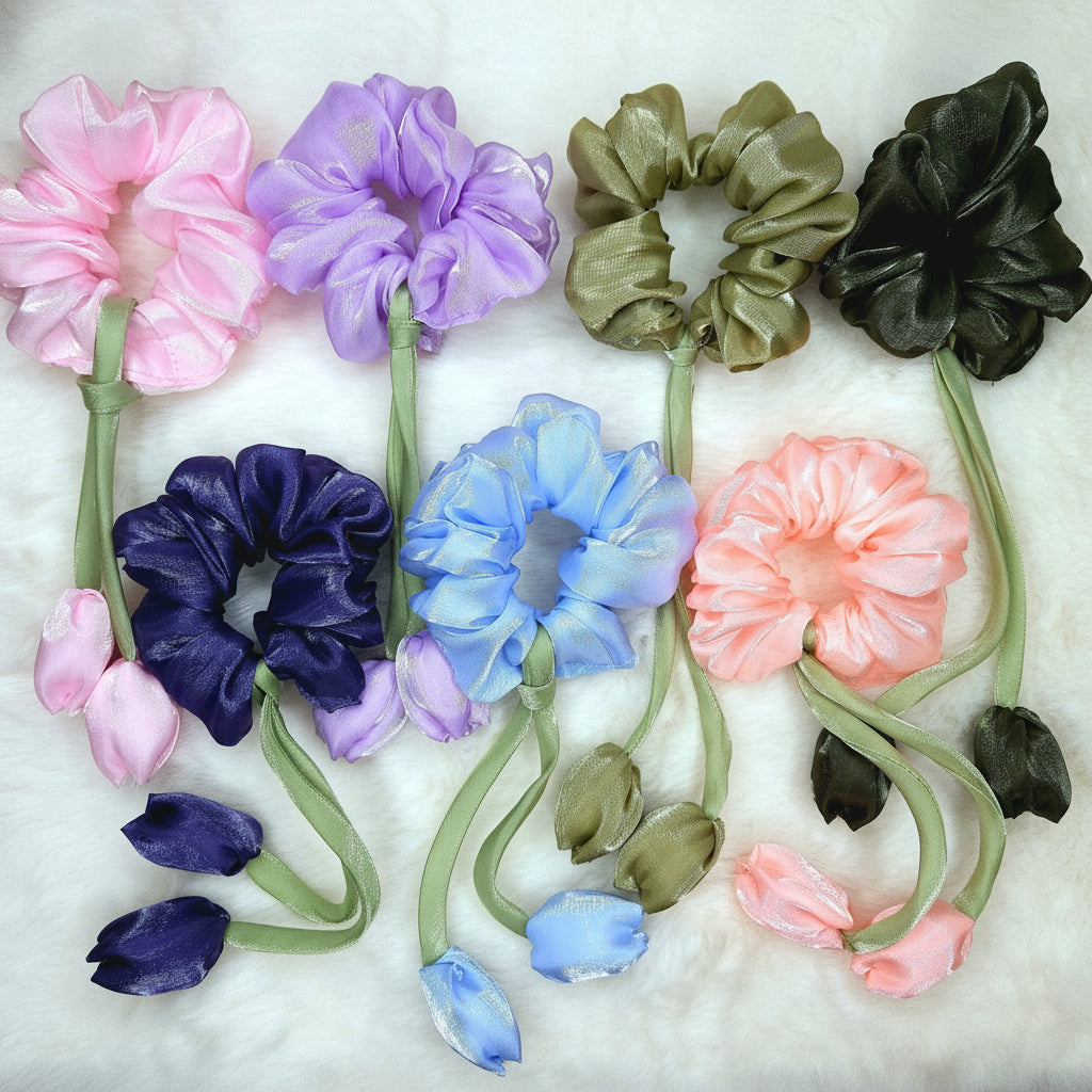 Pastel lavender scrunchies with two tulip buds and green stem ribbons, displayed on white fur background.